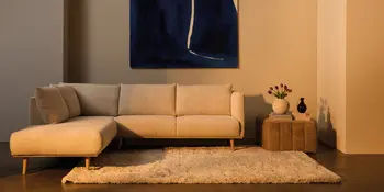 Helles Sofa mit Chaiselongue auf Teppich, Beistelltisch mit Vase und Bild an der Wand